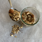 vegan granola on a spoon above a glass dish filled with the granola